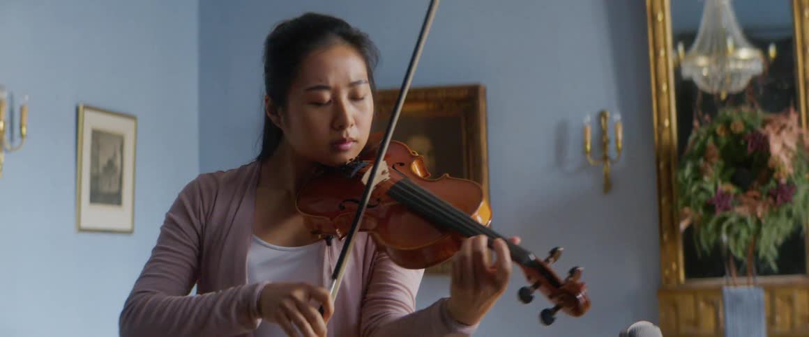 Asian female violinist plays a violin in a large room with paintings