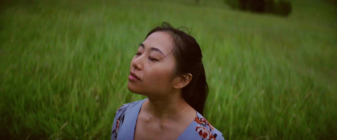 Woman stands in meadow with eyes closed