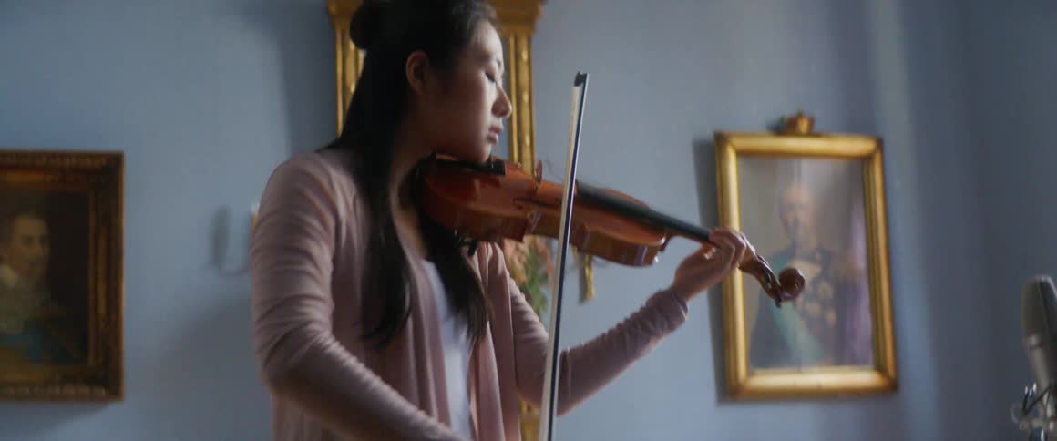 A young woman records herself playing the violin on a laptop at home
