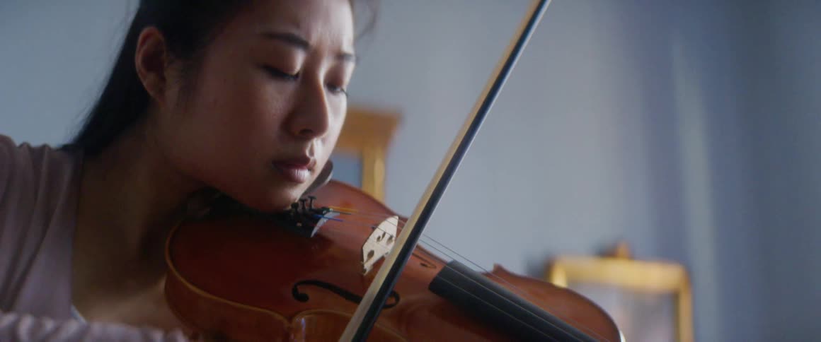 Woman plays string instrument in room with framed art on wall