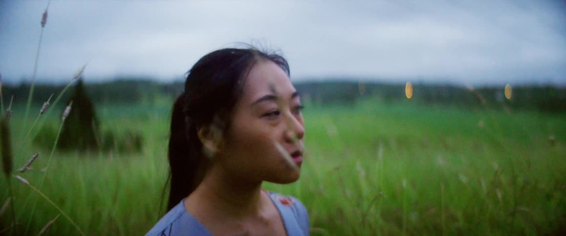 A woman standing in a grassy field with the sky and clouds in the background