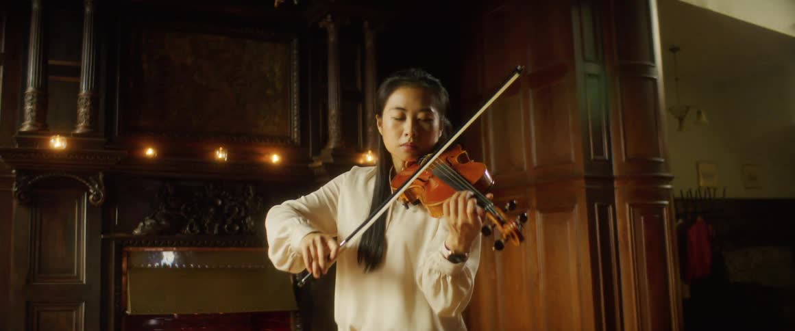 A young asian woman plays the violin alone indoors during the day