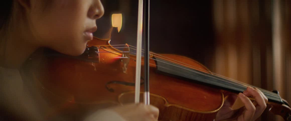 Asian woman holding a violin against her neck and moving a bow plays a violin