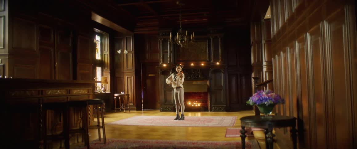Woman plays violin in middle of ornate wood paneled hall near fireplace