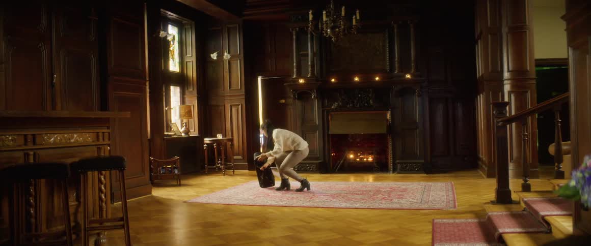 Woman kneels to open musical case set on rug near fireplace in ornate wood paneled room