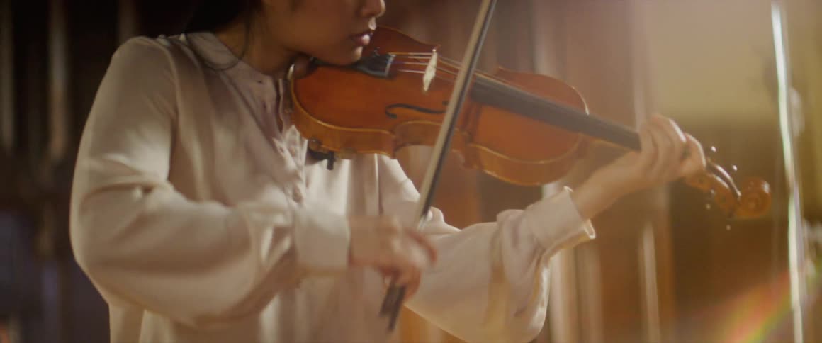 Woman plays violin under ceiling decorated with chandelier