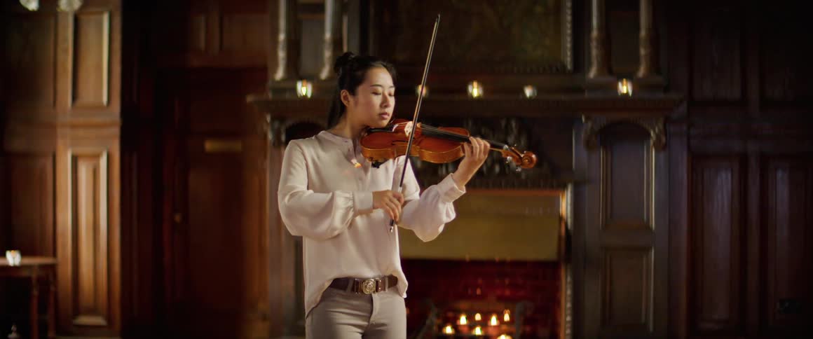 A young asian woman plays the violin indoors during the day