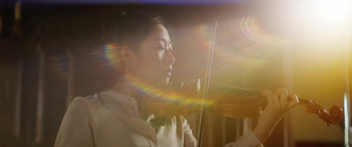 Woman plays violin under bright light near wood paneled wall