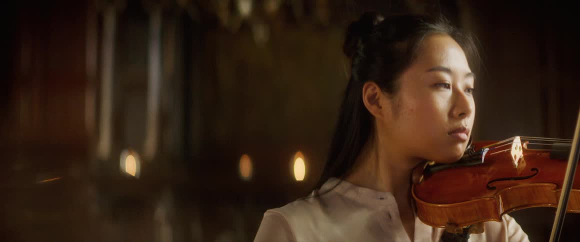 Asian woman holding a violin against her neck and moving a bow plays a violin in a large room