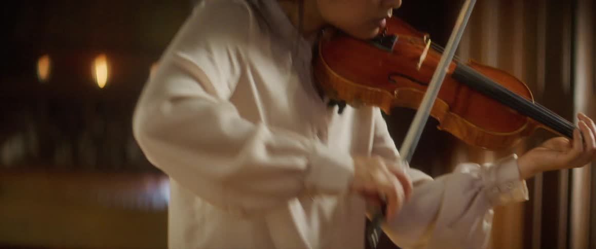 Asian woman holding a violin against her neck and moving a bow plays a violin in a room