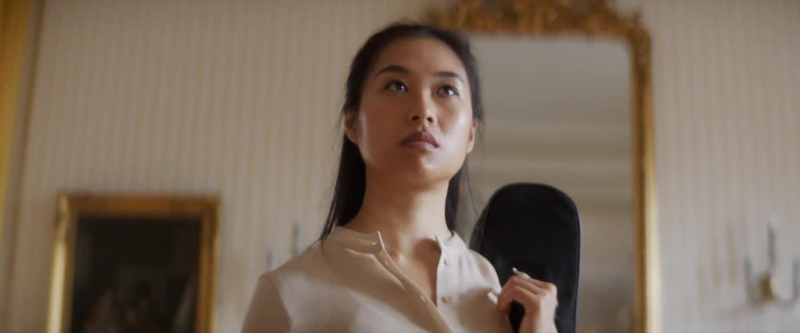 A woman standing in a room holding a violin case with a wall and a mirror in the background