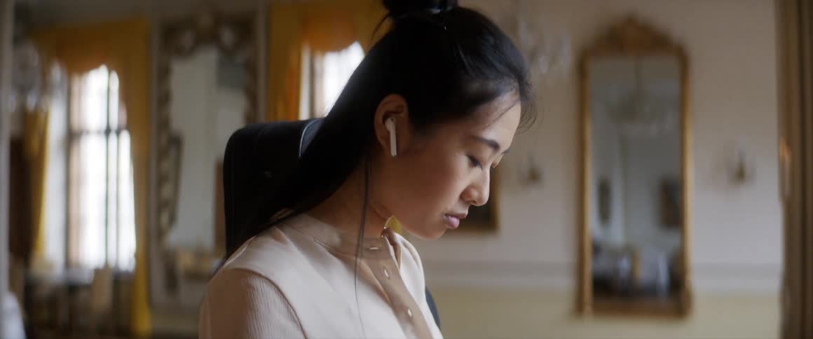 A woman puts in wireless earbuds while standing in a room with a music case on her back