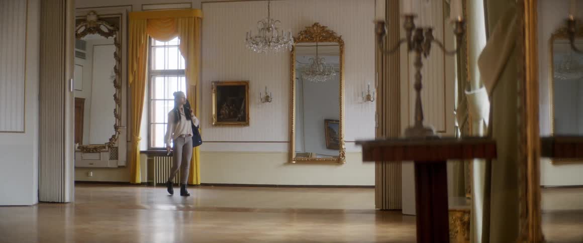 A woman walking in a room holding a violin case with a window and a mirror in the background
