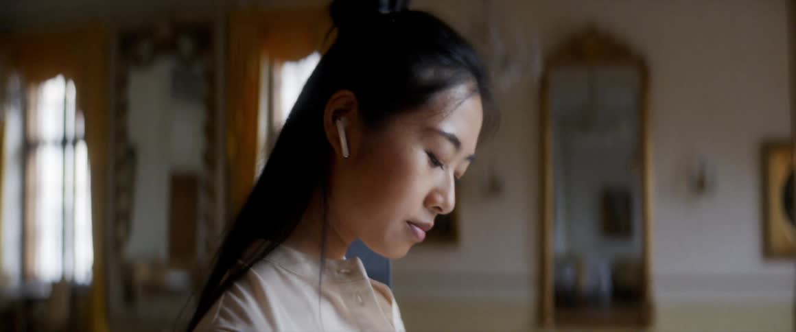 A young asian woman wearing wireless earbuds uses her thumb to tap the screen of her smartphone