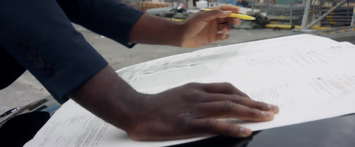 A person with a pen looking at a paper on the hood of a vehicle