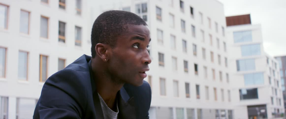 A young man outside an apartment building looks up at it