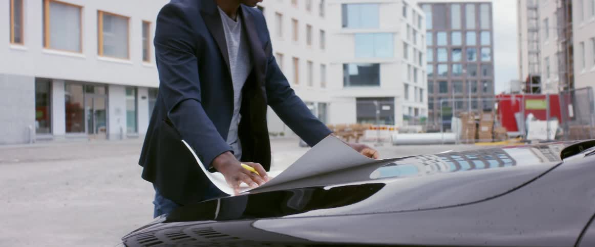A man at a construction site lays out a blueprint on his car and looks at it
