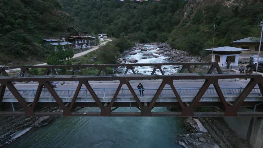 A photographer stands on a bridge over a river in a gorge