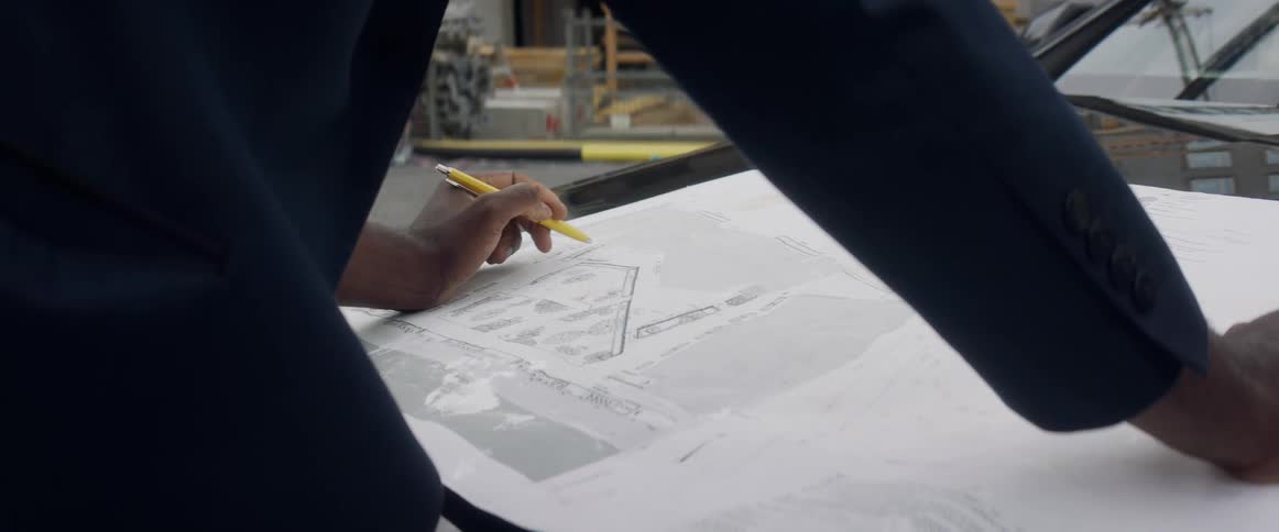A person with a pen looking at a paper on the hood of a vehicle