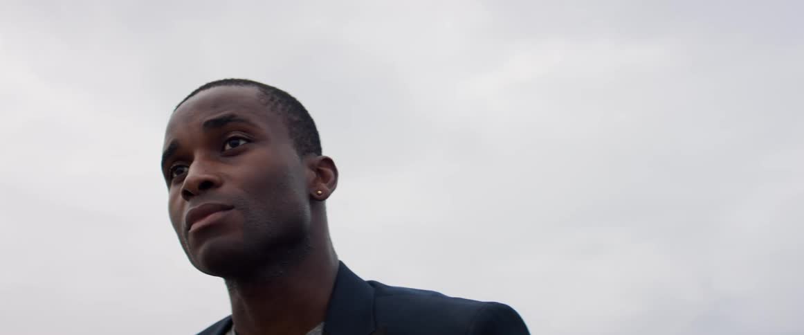 A man stands lost in thought outdoors under a cloudy sky