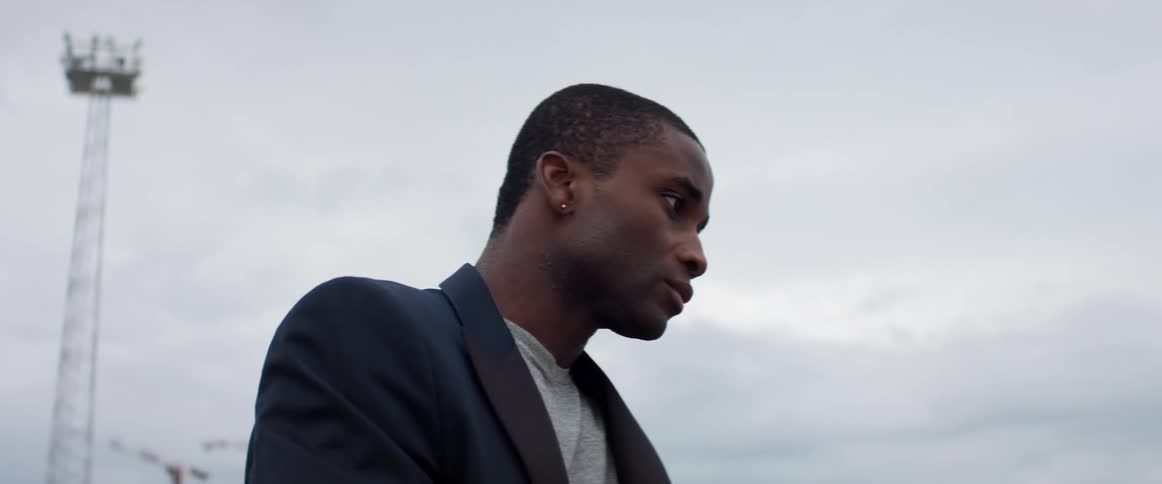A man with a blazer standing with the sky and clouds in the background