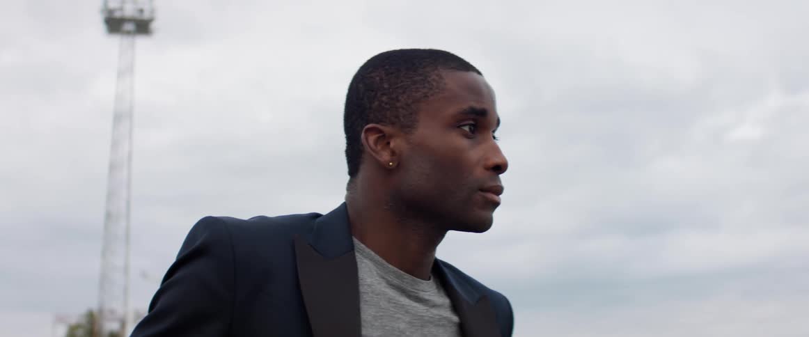 Black man looks off to the side as a tower sits behind him on a cloudy day