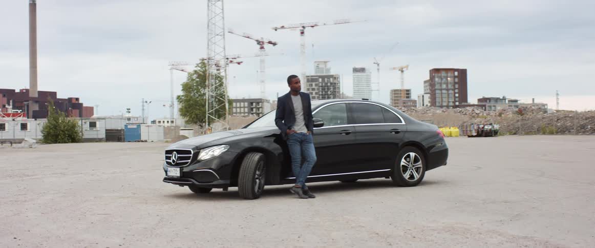 A man casually leans against the side of his luxury automobile