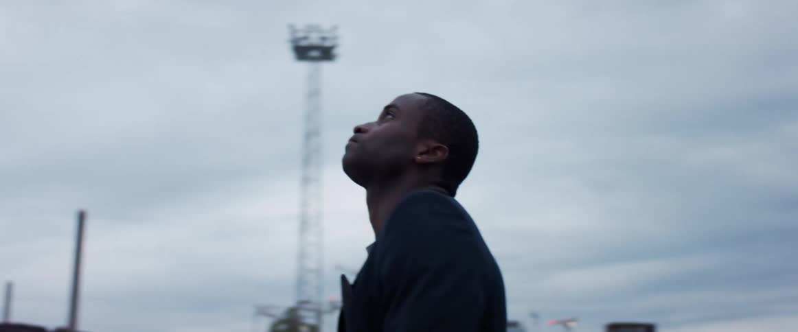 A man stands at a construction site and turns in circles as he rubs his chin and looks up at the sky