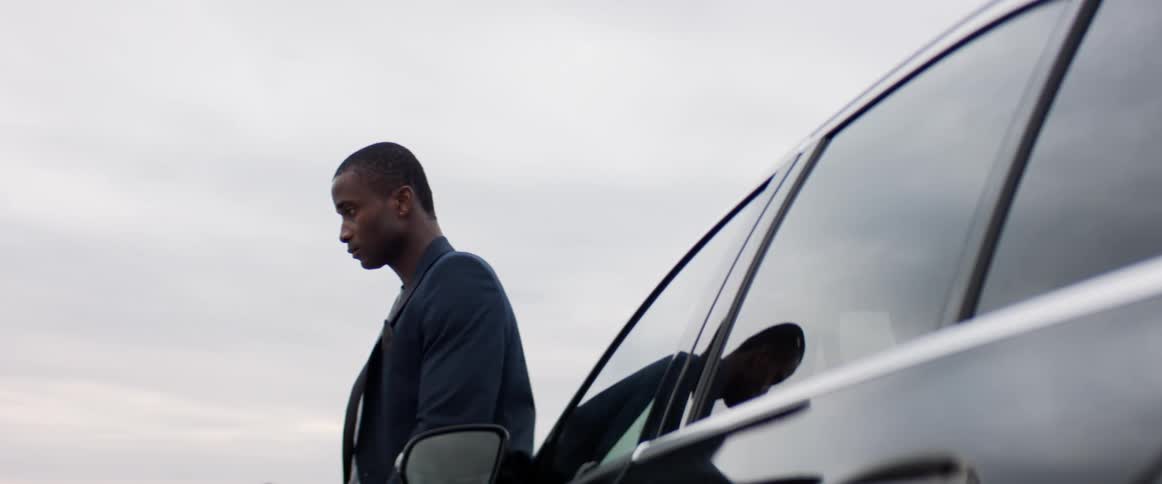 Man leans against black reflective car under cloudy sky