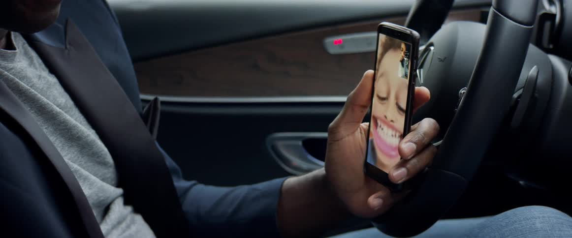 A man sits in his car and facetimes with a child who makes funny faces for the camera