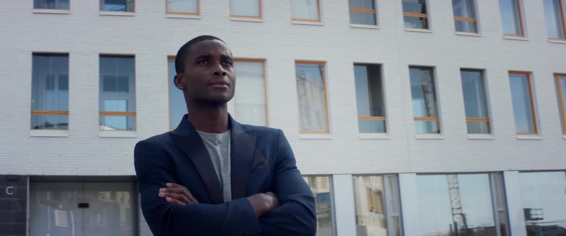A man is standing with his arms folded by the building