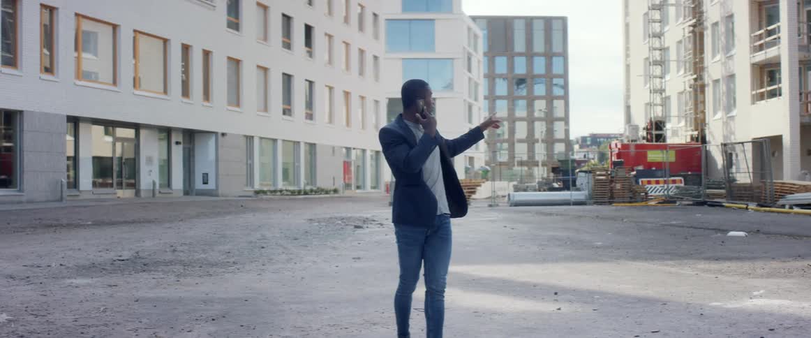 Young man talking on a smartphone in an empty lot under construction in the citys downtown