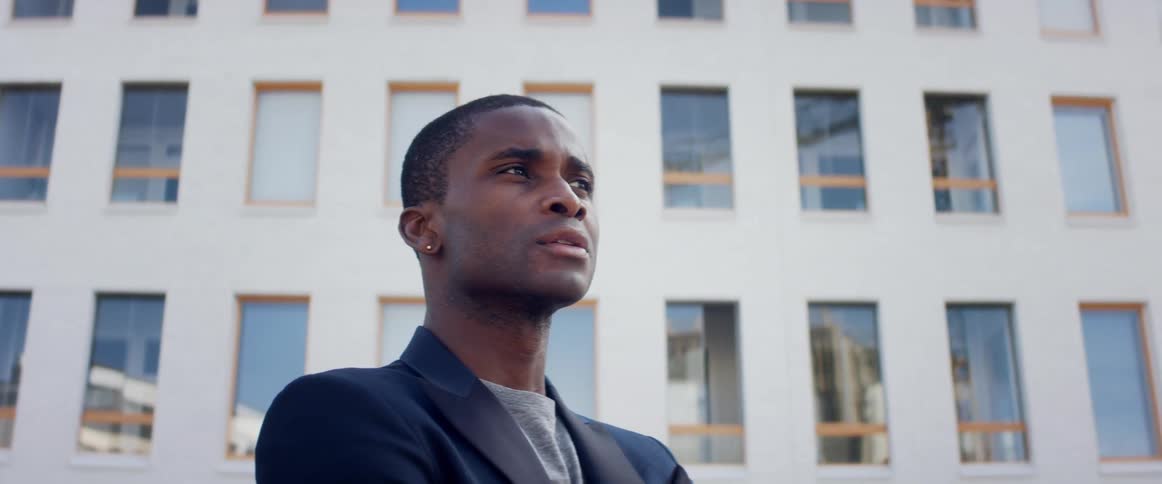 A man standing outdoors in a city on a sunny day gazes around at the buildings surrounding him