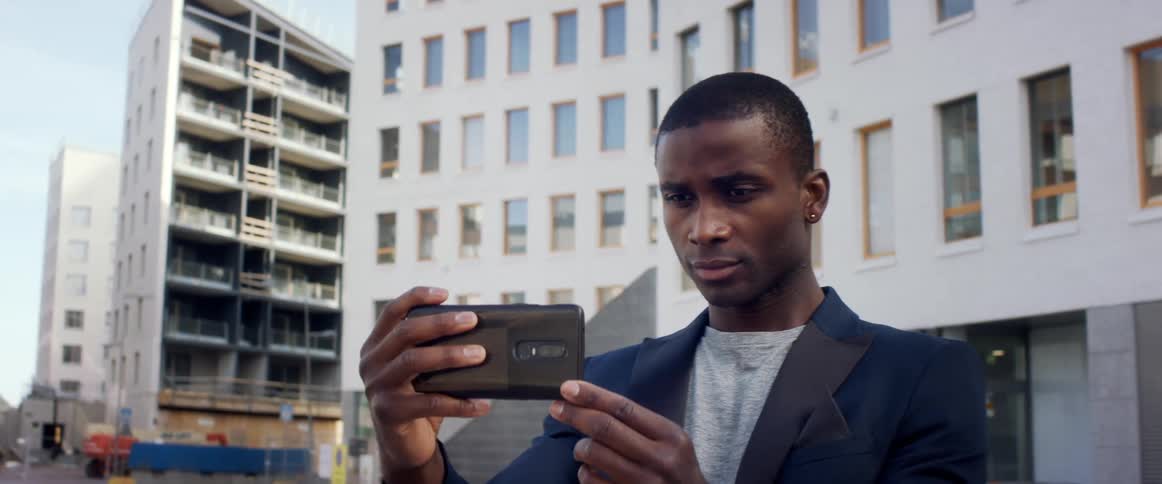 A man standing in front of an apartment building takes a selfie on his phone
