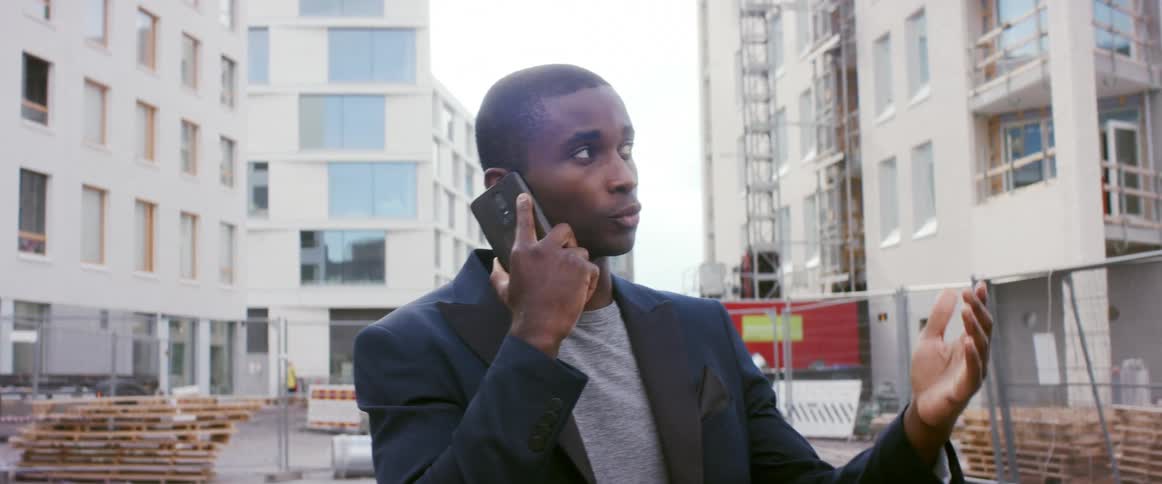 A man talks on a smartphone while standing on a construction site in a metropolis during the day