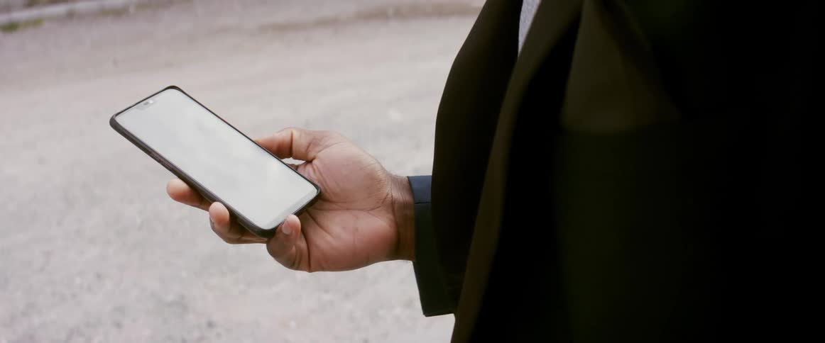 A man stands in the middle of a gravel road and looks at his phone