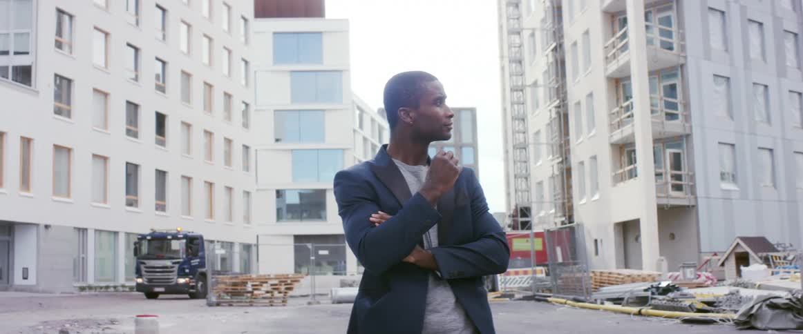 A man stands in front of a construction site in a city street and looks around