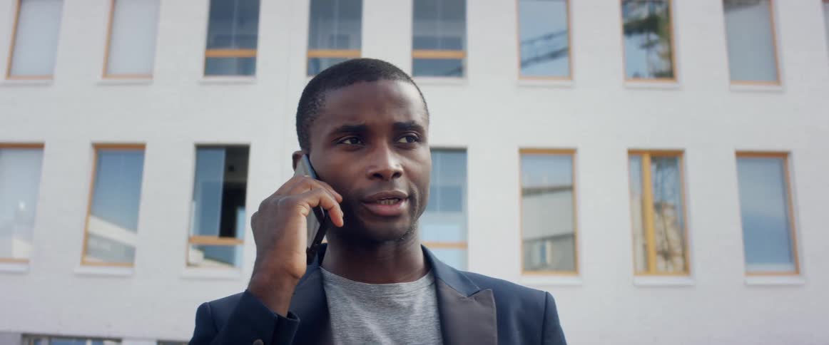 Young man in a business suit talking on the smartphone near a building at day