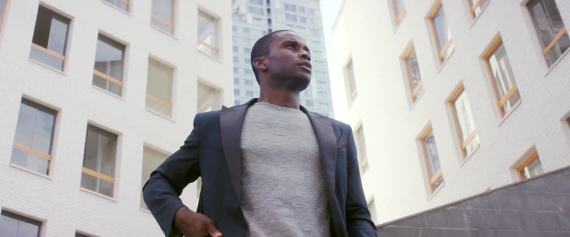 A young man in front of apartment buildings talks on his cell phone and then hangs up and looks around