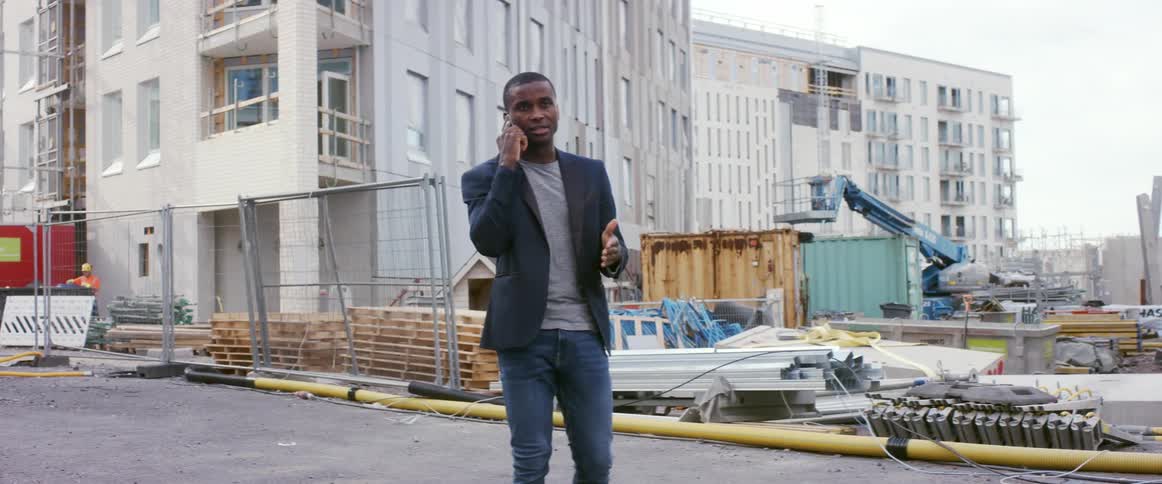 A man talks on the phone while standing on a construction site for apartment buildings