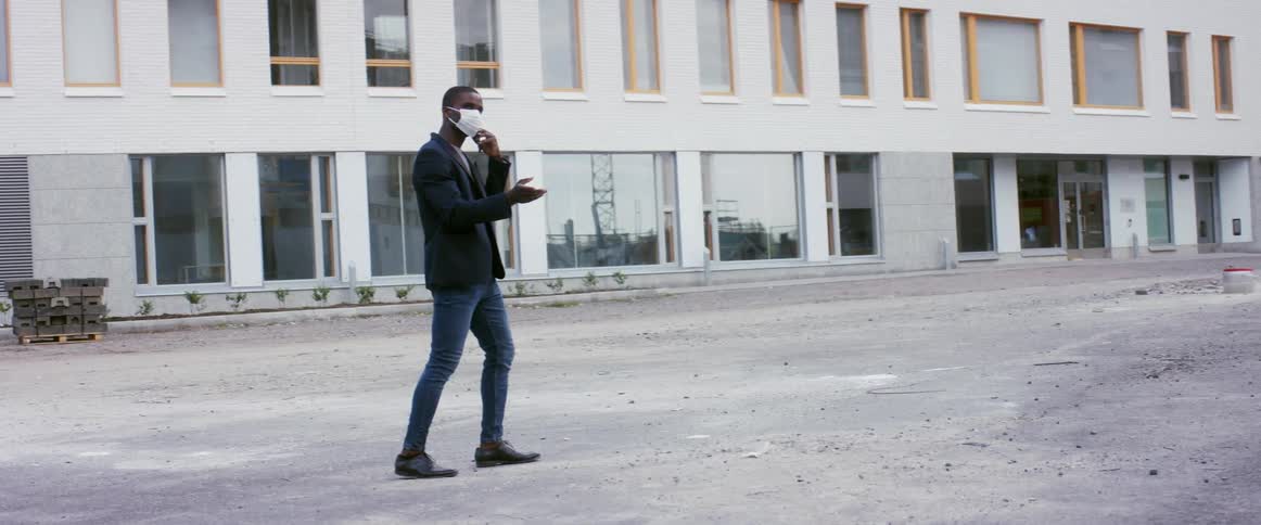 A man with a mask talking on a smartphone with a building and windows in the background