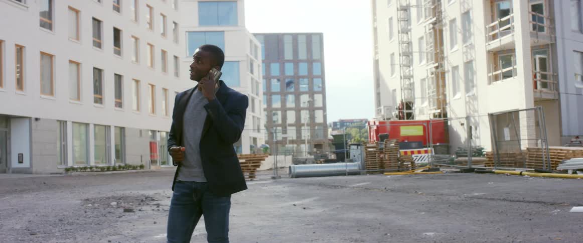 A man standing in front of construction at apartment buildings talks on his cell phone as he looks around