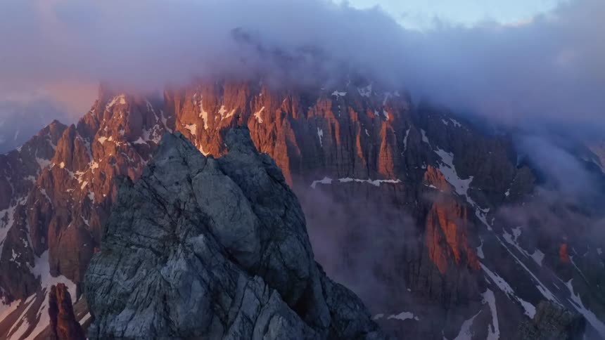 Cross sits on peak in fog covered mountainous terrain speckled with snow