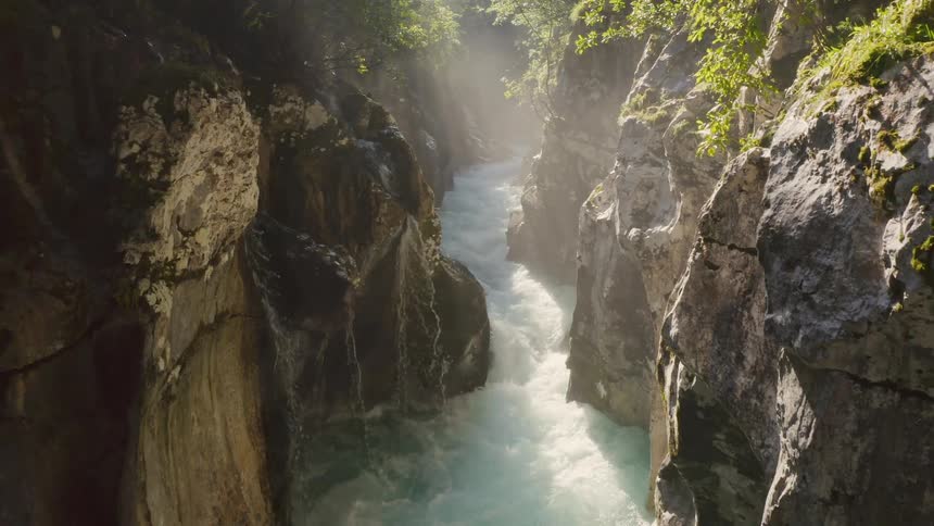 Narrow streams of water fall into river flowing between cliff walls forming rapids