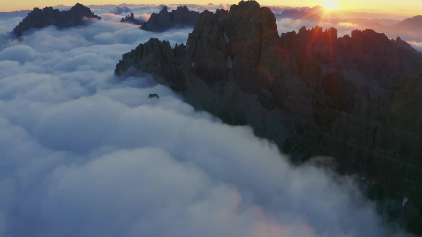 The summit of a mountain ridge peaks up through a sea of clouds under the low evening sun