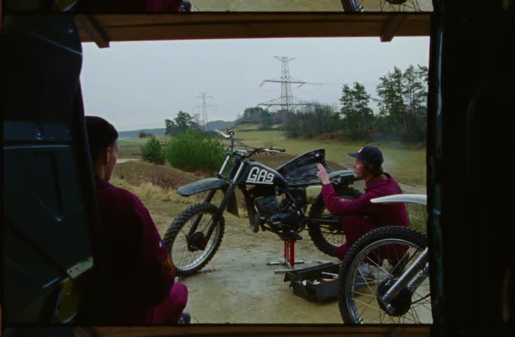 Two males one smoking sitting at there van with there dirtbikes