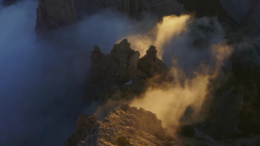 Sun brightens part of low lying clouds leaving rest in shadow around mountain peak and ridges