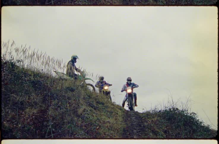 A group of motocross riders stop atop a hill for a moment before riding down