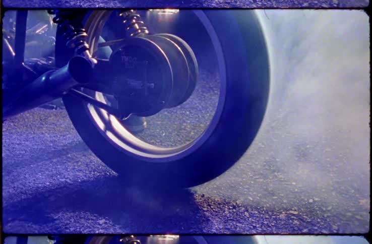 Person in jeans stands near motorcycle spinning on road creating smoke