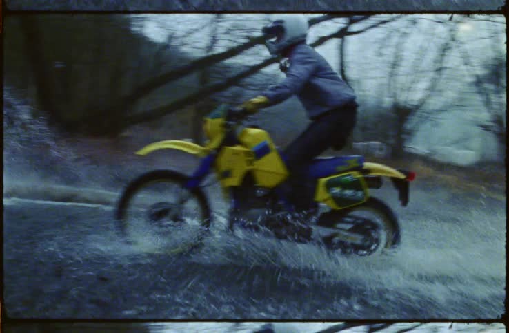 A filmstrip of two people riding motorbikes through a large puddle in a forest